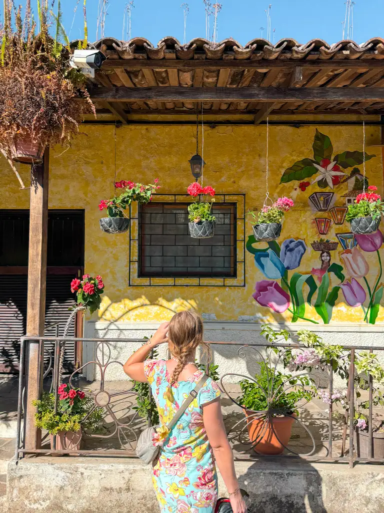 a girl stands in front of a painted house in the salvadoran highlands