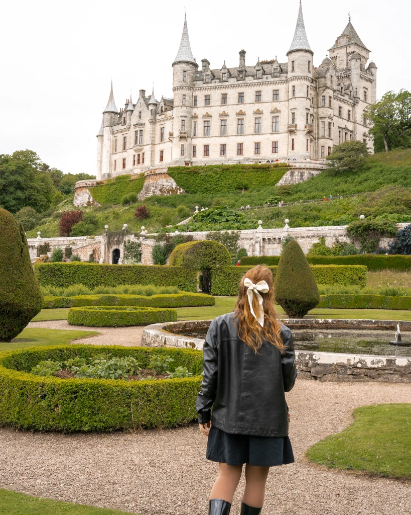 girl stands with a white bow and black dress in the palace gardens of dunrobin castle, scotland