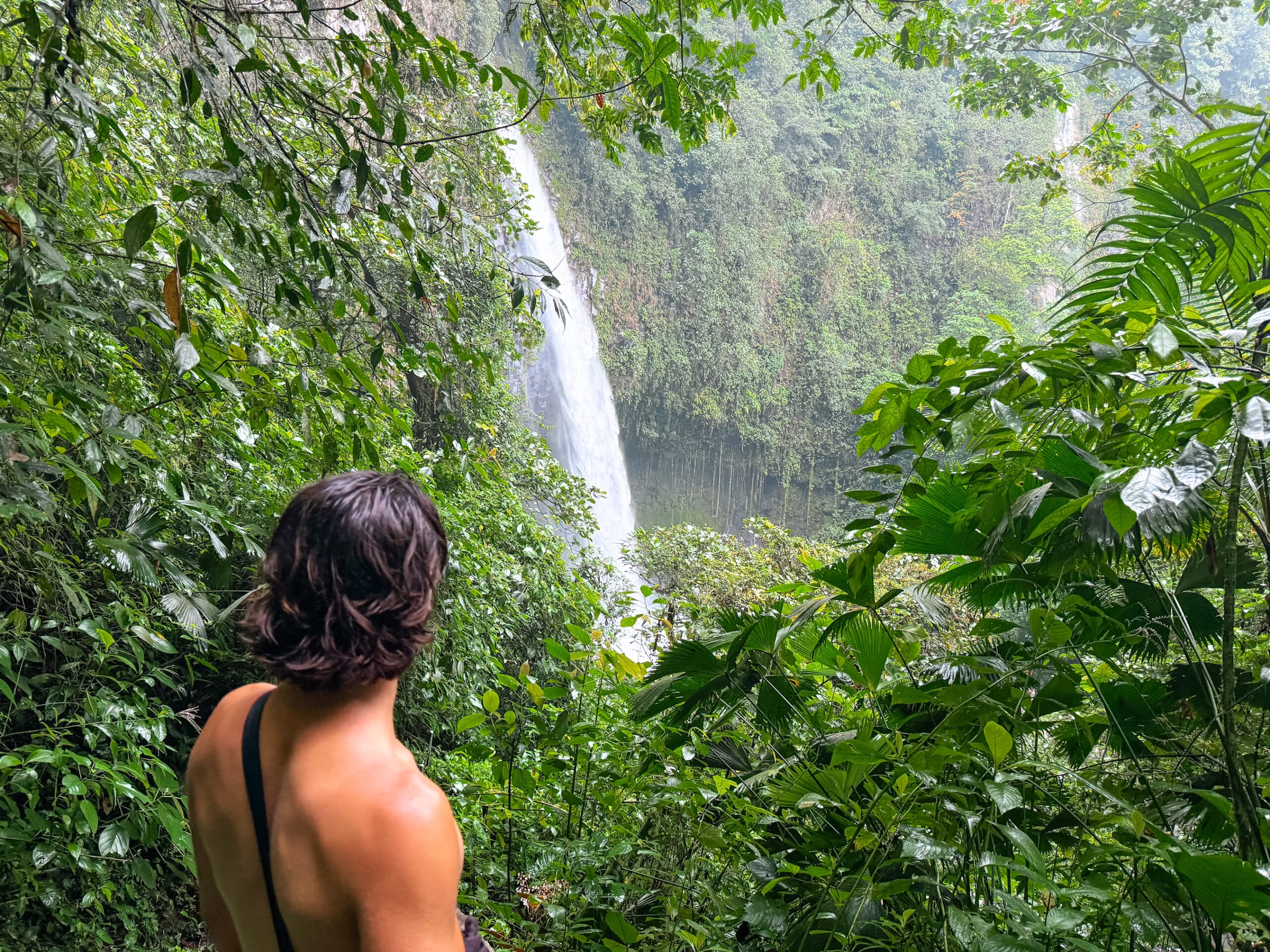 costa rica travel la fortuna waterfall with man looking on from the jungle