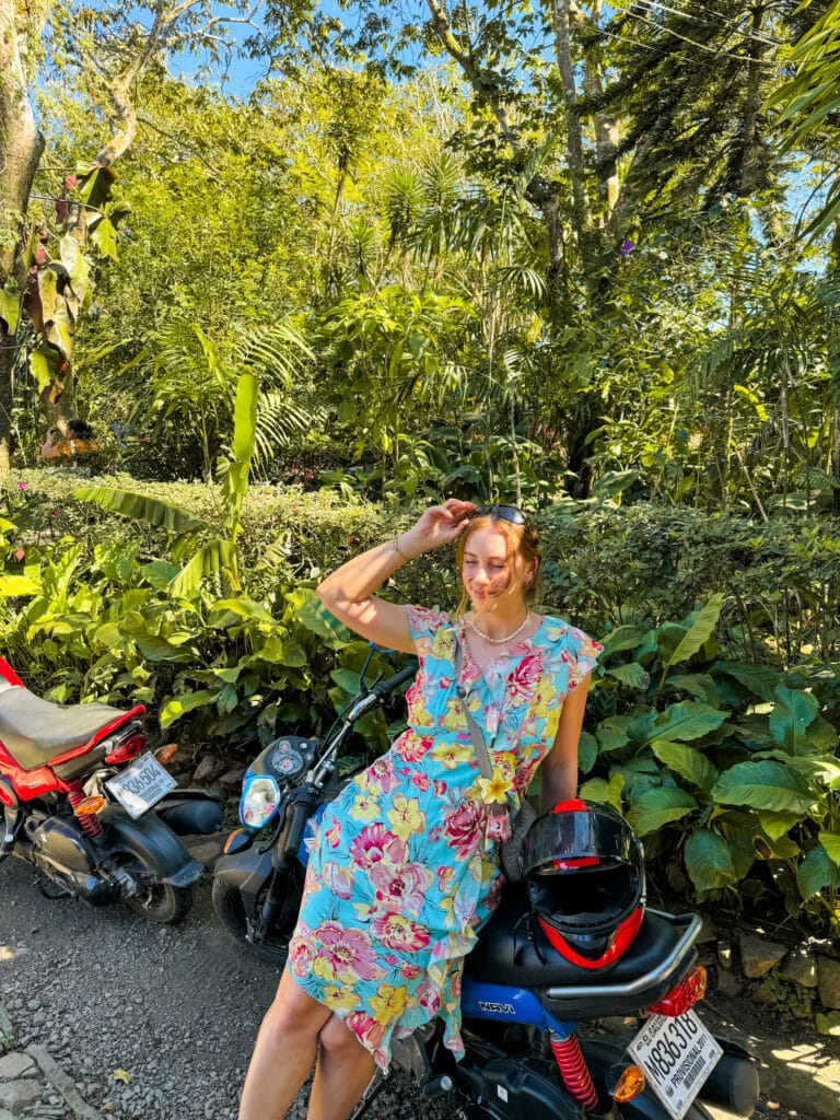 girl rests on motorbike in floral dress in jungle