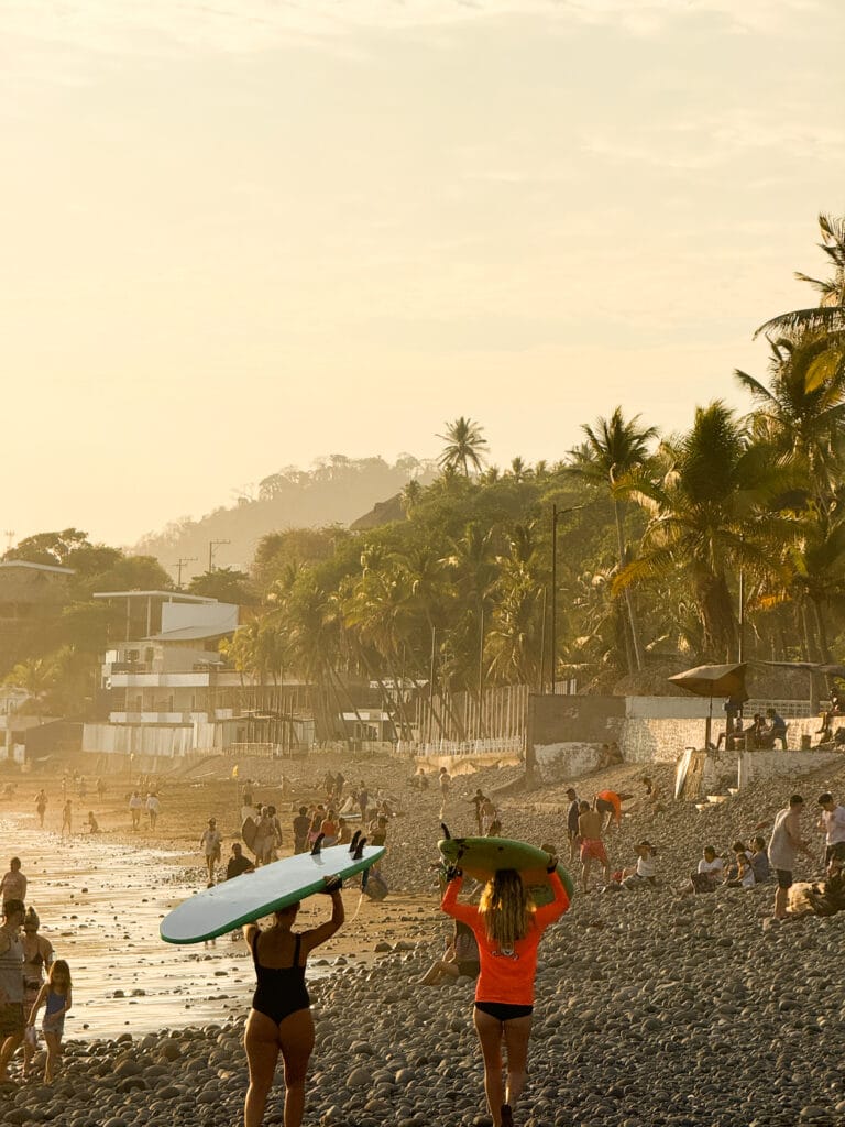 two women holding surfboards and walking into the sunset in el salvador beach