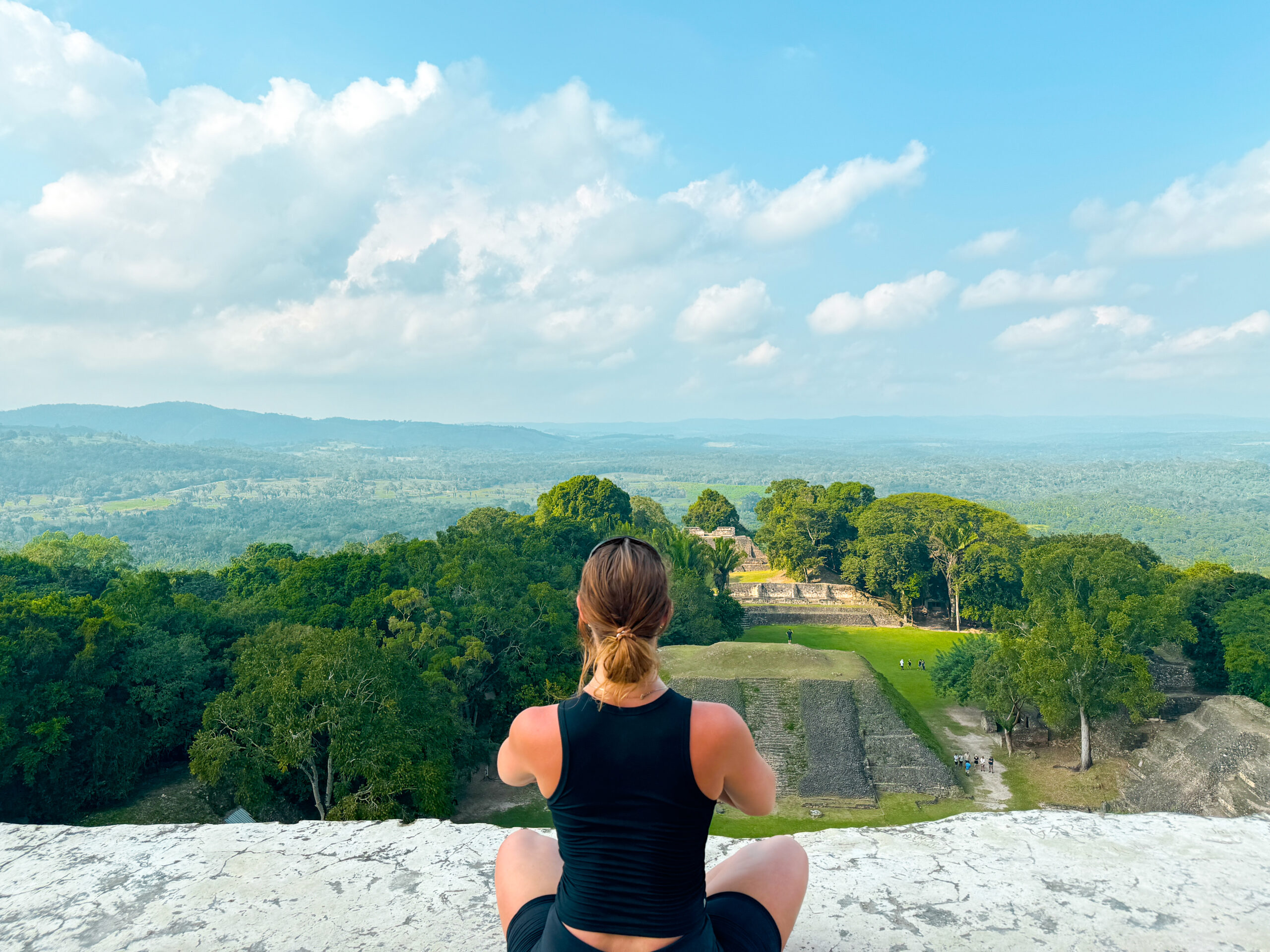 girl sits on top of mayan ruin temple and looks at the view of jungle in belize